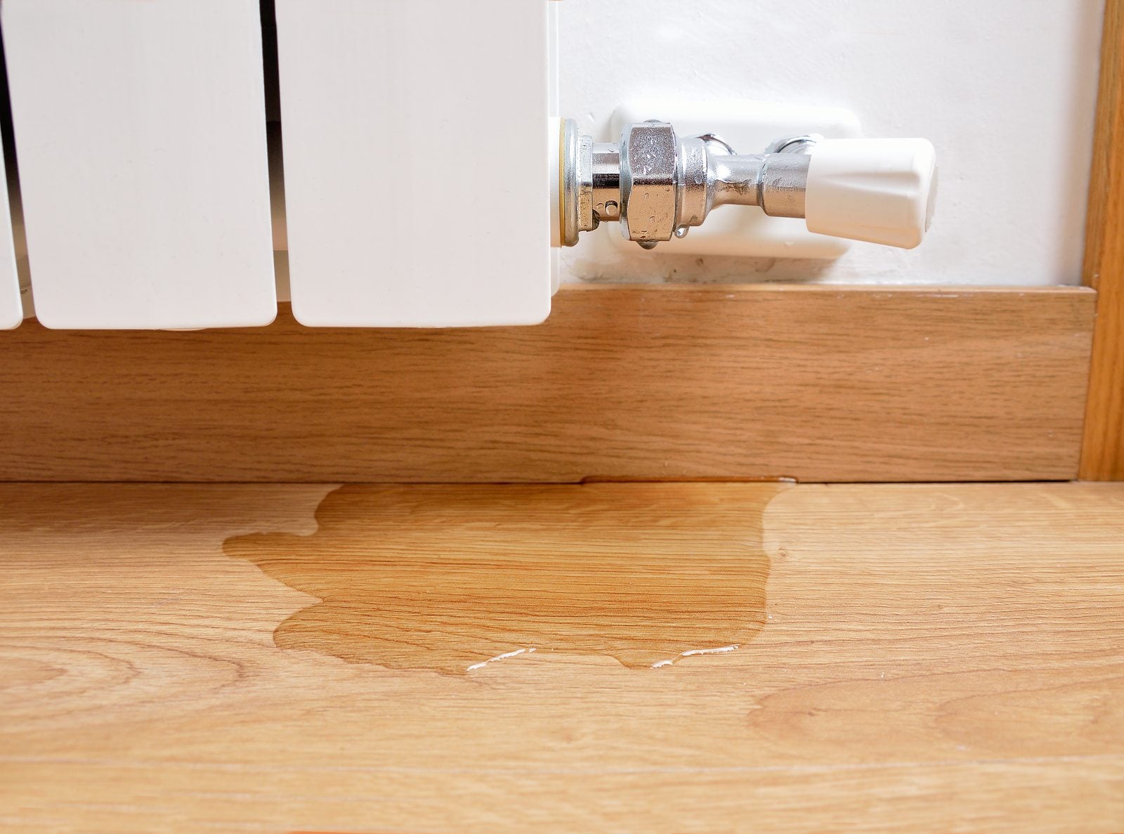 Water puddle on a wood floor below a radiator valve